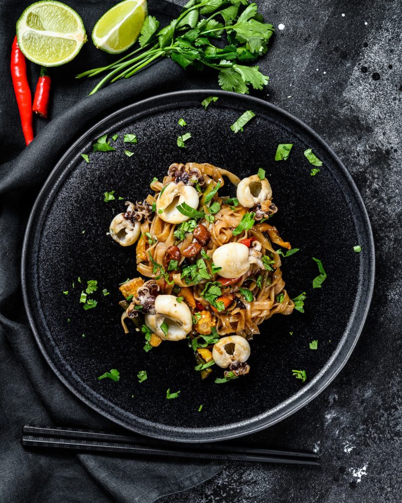 homemade-stir-fry-damage-noodles-with-seafood-and-vegetables-in-a-plate-black-background-top-view.jpg